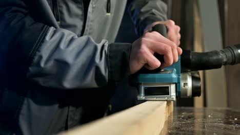 close-up of a carpenter's hand working with an electric plane in a home workshop