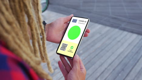 man with dreadlocks holding smartphone, covid vaccination certificate, eu flag and qr code on screen