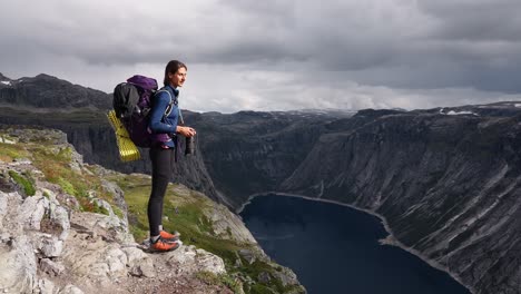 woman hiker stands on cliff edge in norway, looking over deep fjord valley view