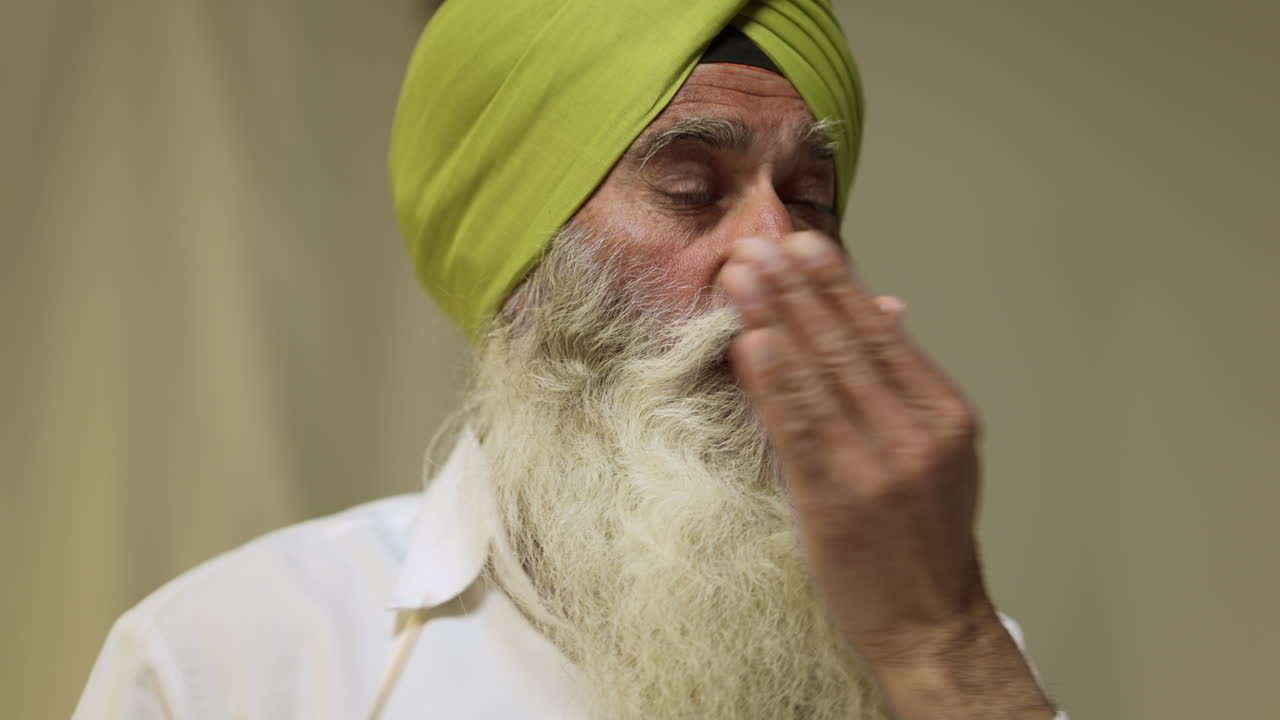 수염을 가진 시크교 신자의 스튜디오 은 평평한 배경에 터반을 입을 때 살라이 바늘을 사용합니다.