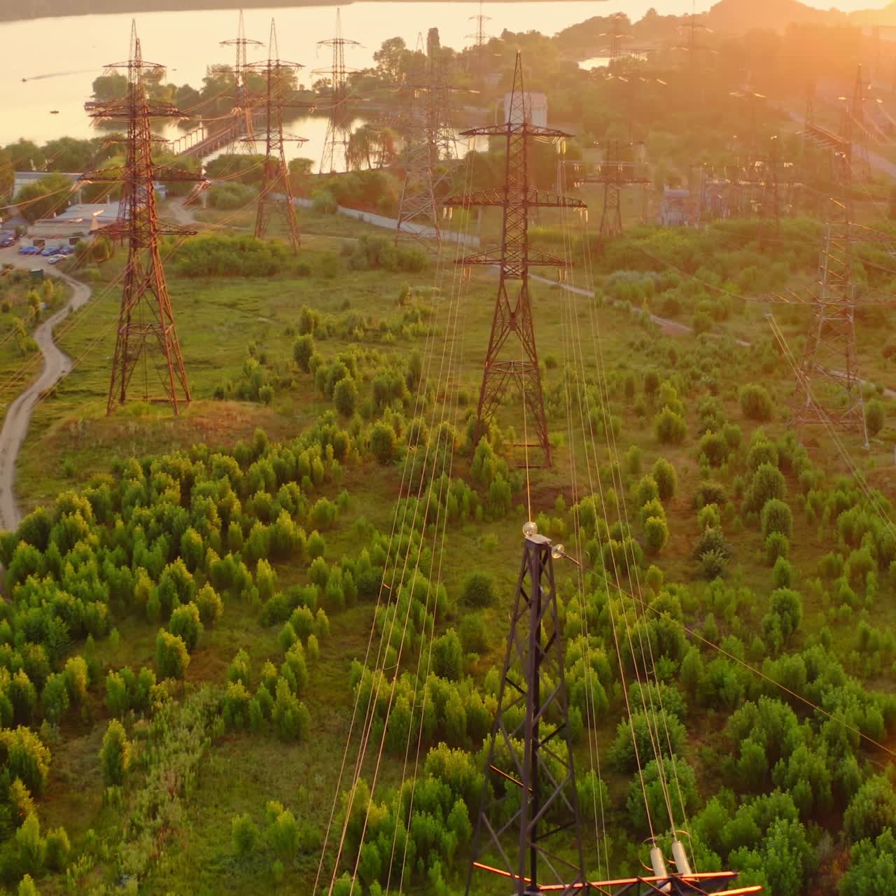 Power line pylons near the river. Electric towers with electric cables with high voltage current. Flight over the transmission lines in the evening. Aerial view.