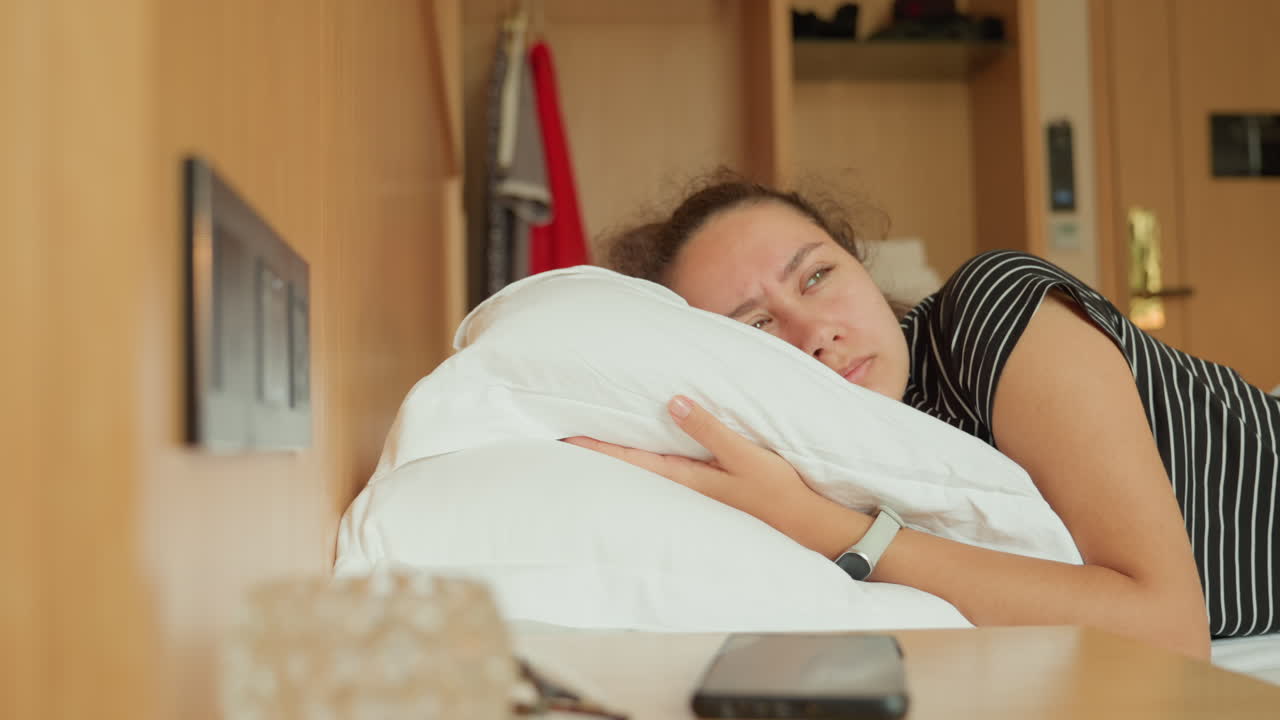 Caucasian woman resting on hotel desk pillow during daytime, corporate traveler naps between meetings, clutching plush pillow, smartwatch visible, smartphone and glasses on wood desk, warm natural