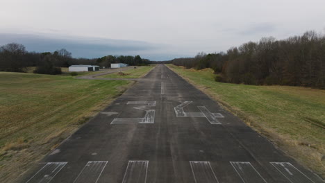 small, decommissioned runway, airport in rural arkansas, aerial flying low over faded markings on cement