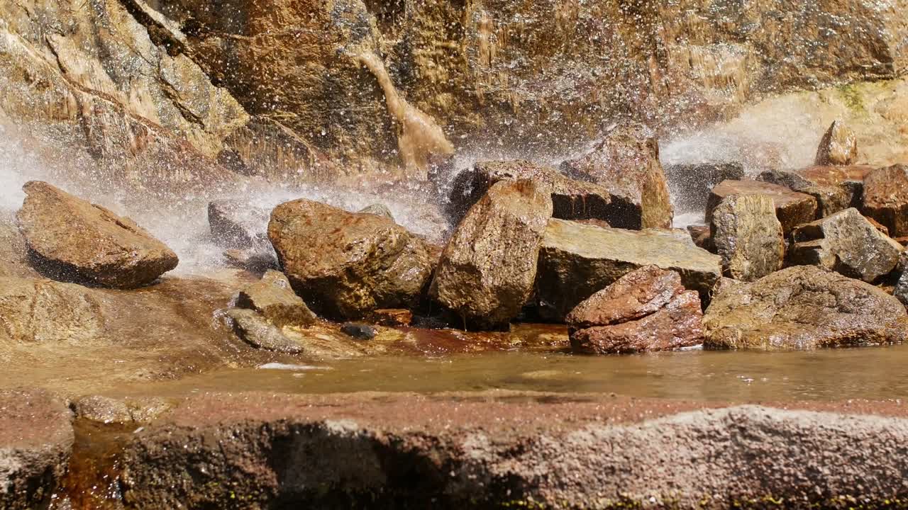 Beautiful waterfall from a cliff in the forest. 4K video of flowing water, flowing stream among stones. Stream in the forest