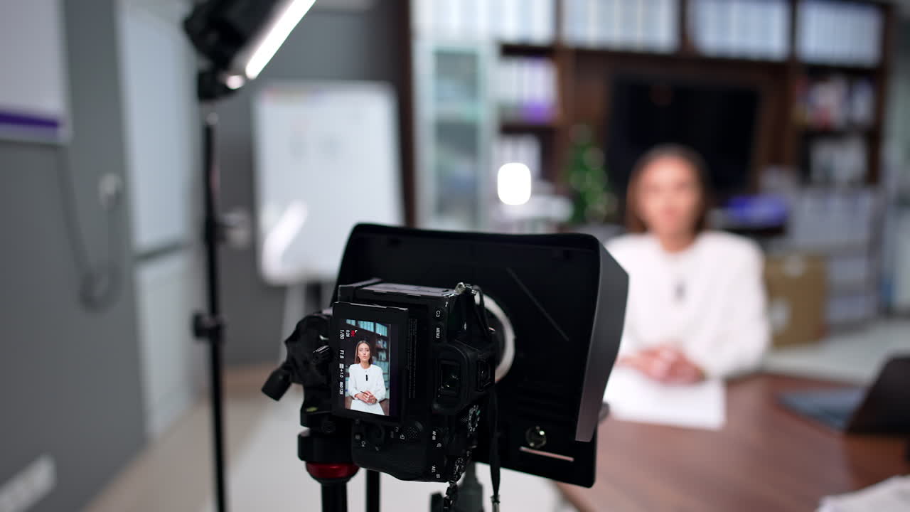 Brunette woman in white jacket records video on professional camera. Close up view of the blogger's equipment.