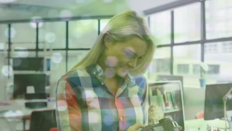 Animation-of-light-spots-over-smiling-caucasian-businesswoman-using-computer