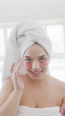 vertical video of happy caucasian plus size woman applying under-eye patches in slow motion