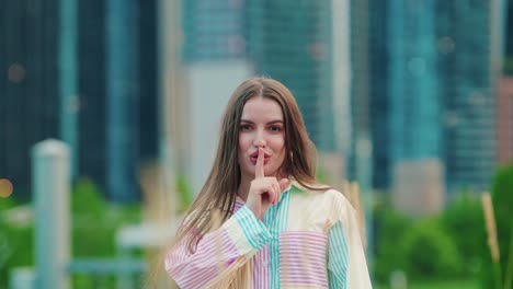 caucasian pretty lady looking at camera makes gesture silence sign pretends to close zip up mouth keep secret information silent outside with a corporate feeling - chicago skyscrapers background