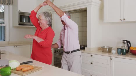 Feliz-Pareja-De-Ancianos-Caucásicos-Divirtiéndose-Bailando-En-La-Cocina-Mientras-Preparan-La-Comida