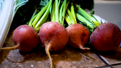 close up pan of raw red beets with green stems next to bok choi cabbage