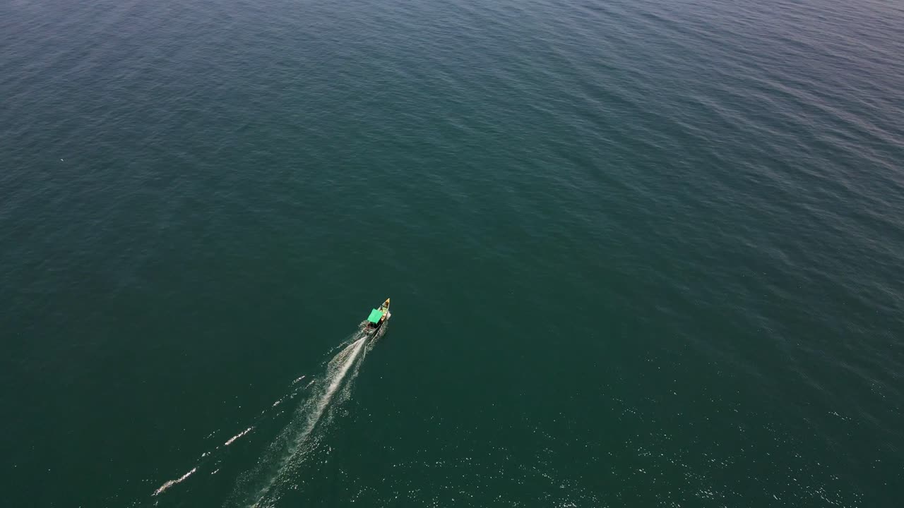 Top-down aerial drone shot of a fishing boat in the center of the calm, deep blue ocean waters.