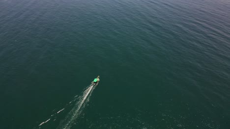 top-down aerial drone shot of a fishing boat in the center of the calm, deep blue ocean waters.