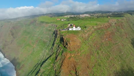 Ponto-do-Pargo-lighthouse-on-a-green-hill-mountain-with-sea-waves-below