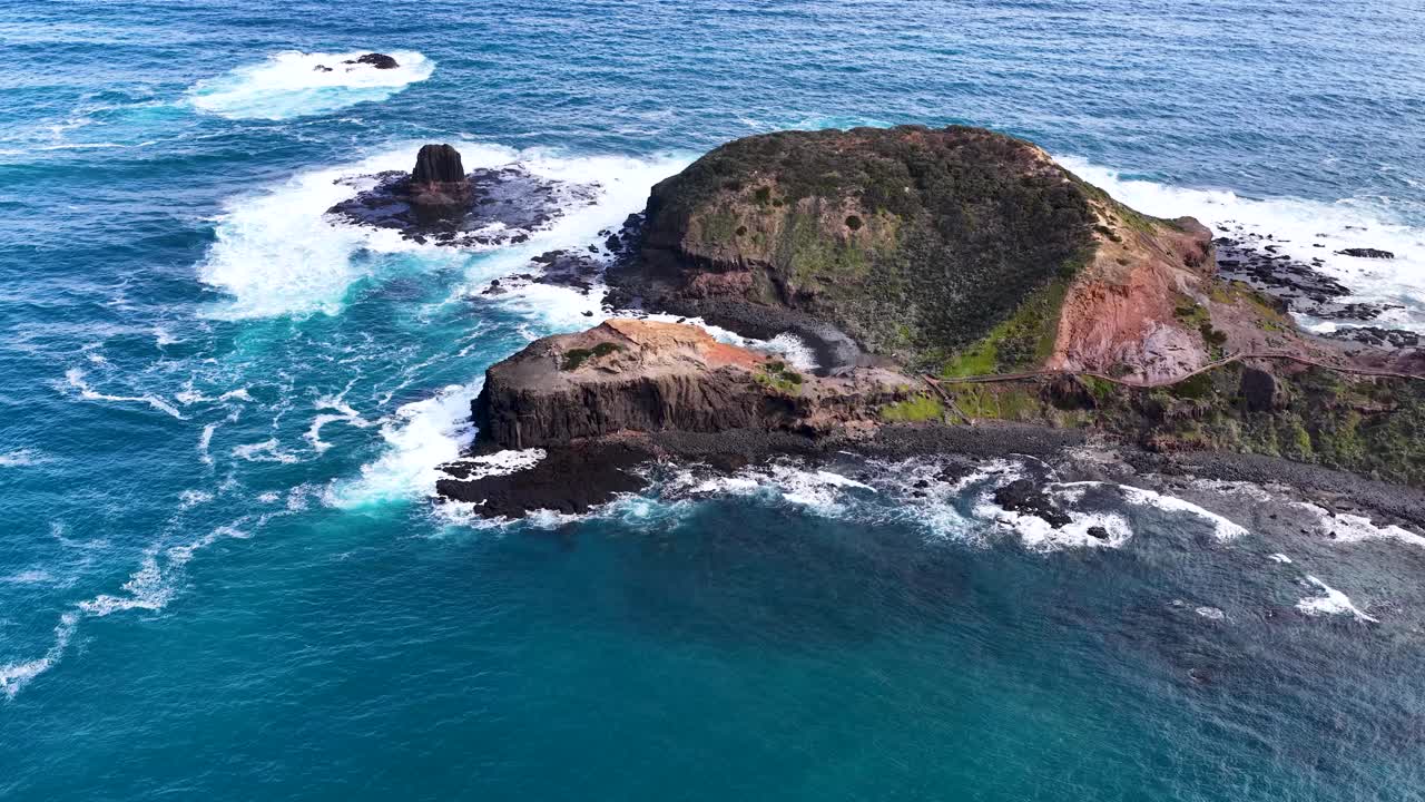 Drone camera glides above rugged island, turquoise ocean waves, and dramatic rocky coastline in daylight