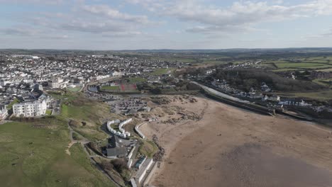 Wide aerial panorama of Bude where river mouth, dunes and pastel townhouses meet rolling hills and Atlantic breakers, conveying vibrant Cornish coastal lifestyle