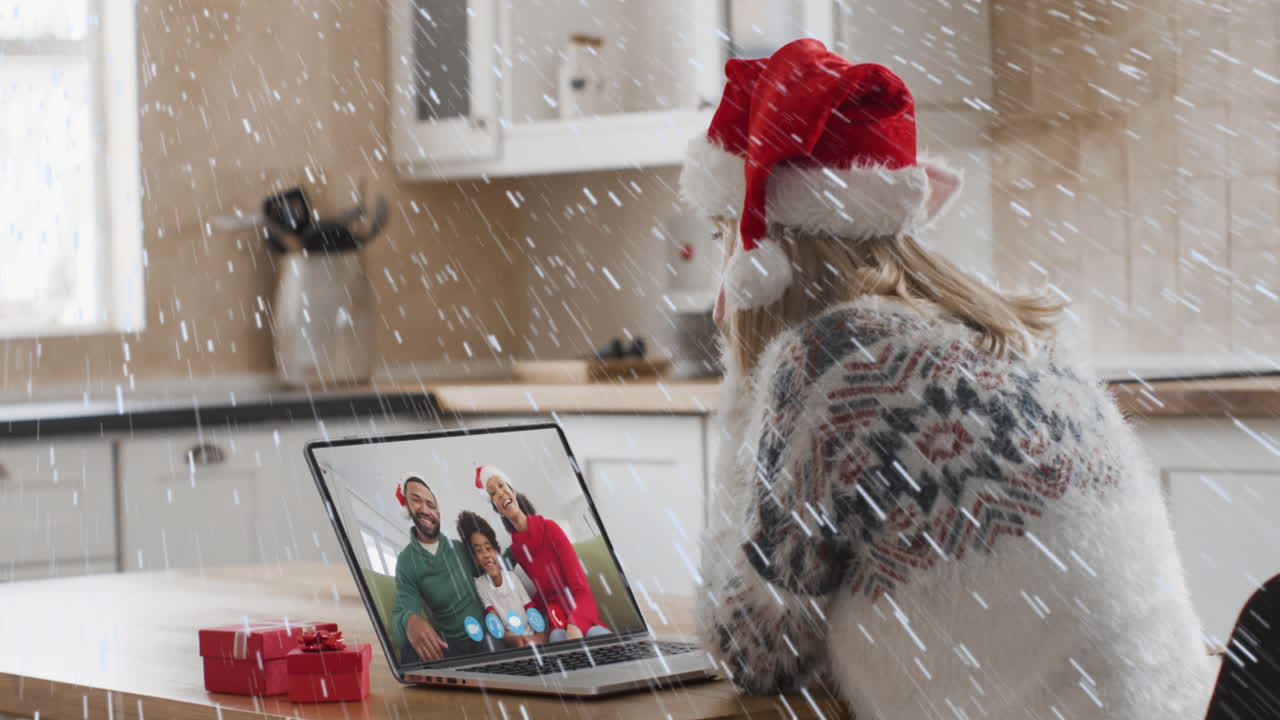 animación de nieve cayendo sobre mujer caucásica en sombrero de santa en llamada de video portátil con su familia