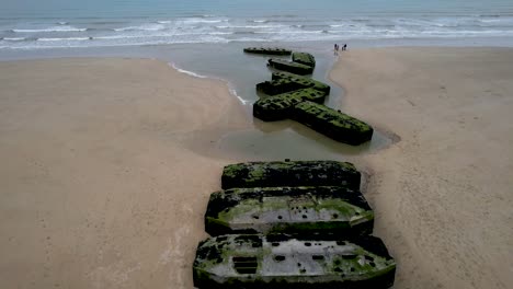 people standing on normandy beach next to world war 2 bunker ruins