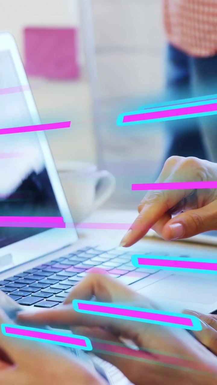 Video verticale: Donna che indica un laptop mentre un collega digita, con strisce al neon che facilitano la revisione dei dati.