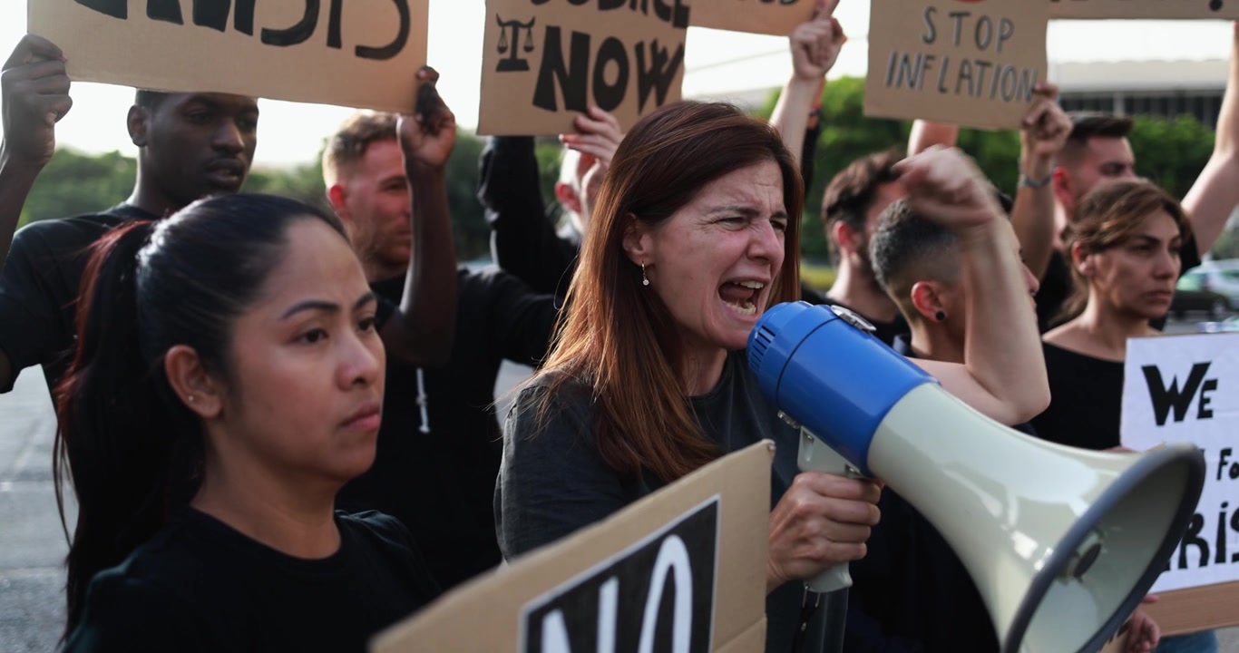Donna che urla in un megafono a una protesta con una folla eterogenea