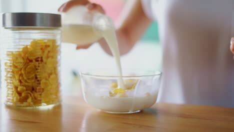 preparing cereals breakfast on kitchen table. close up woman hands pouring milk