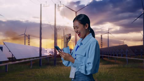 side view of asian female professional worker with her smartphone with solar panel and wind turbines, she raises her fist up with screaming goal after check on the smartphone