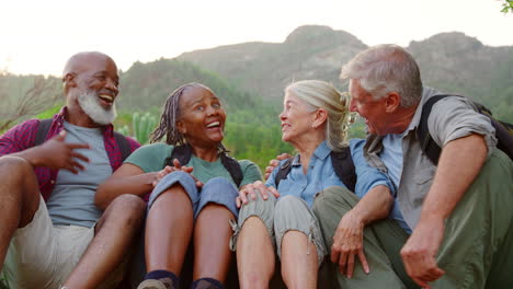 Active-Senior-Friends-Sitting-Taking-A-Break-Hiking-Through-Countryside-Together