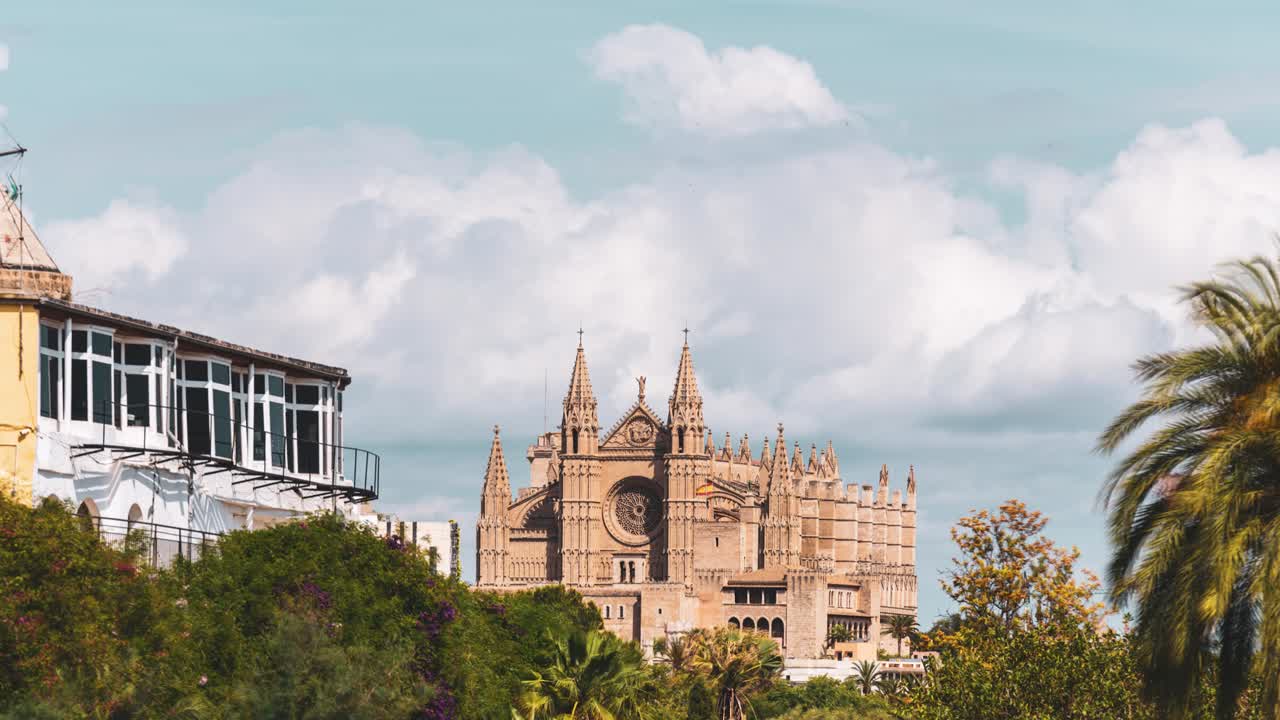 Timelapse of the Palma Cathedral with colorful houses in scene (Palma, Mallorca, Spain).
Palma Cathedral framed with palm trees and windmill against a soft sky backdrop and developing storm clouds.