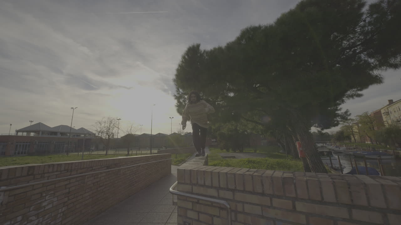 Urban park scene with person jumping over wall and person sitting on wall