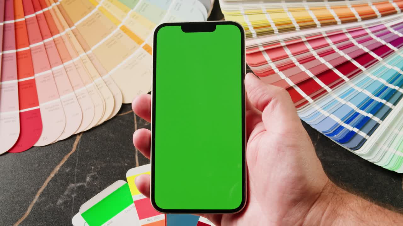 mano sosteniendo un teléfono inteligente con pantalla verde sobre muestras de color