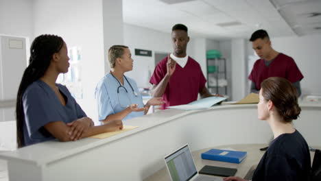 diverse male and female doctors discussing work at reception desk at hospital, slow motion