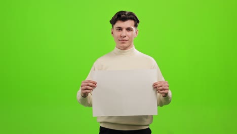 el hombre está de pie y mirando a la cámara. está sosteniendo un papel blanco y sonriendo. está de pie sobre un fondo verde. pantalla verde. 4k.