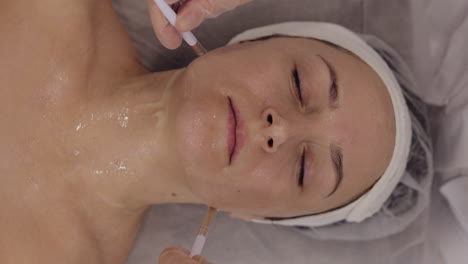 enzyme therapy beautician applying moisturizing medical cream on middle-aged woman face with brushes