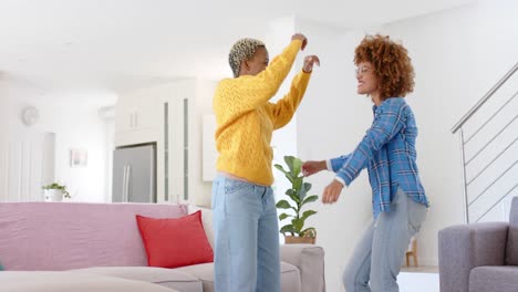 happy diverse female lesbian couple dancing in living room in slow motion