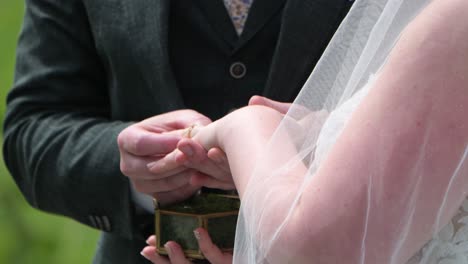 groom places wedding ring on bride's finger during outdoor ceremony