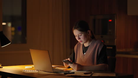 beautiful woman working late at home using a laptop and receiving text messages on smartphone. hands of woman texting message on mobile smart phone for communication and chatting on social online