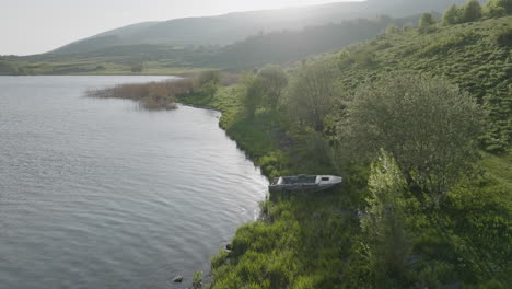 an abandoned motorboat on the shoreline of a calm lake in the early morning