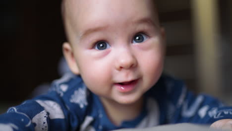 beautiful caucasian child lying on his belly. baby boy in blue clothes smiles to the camera. close up.