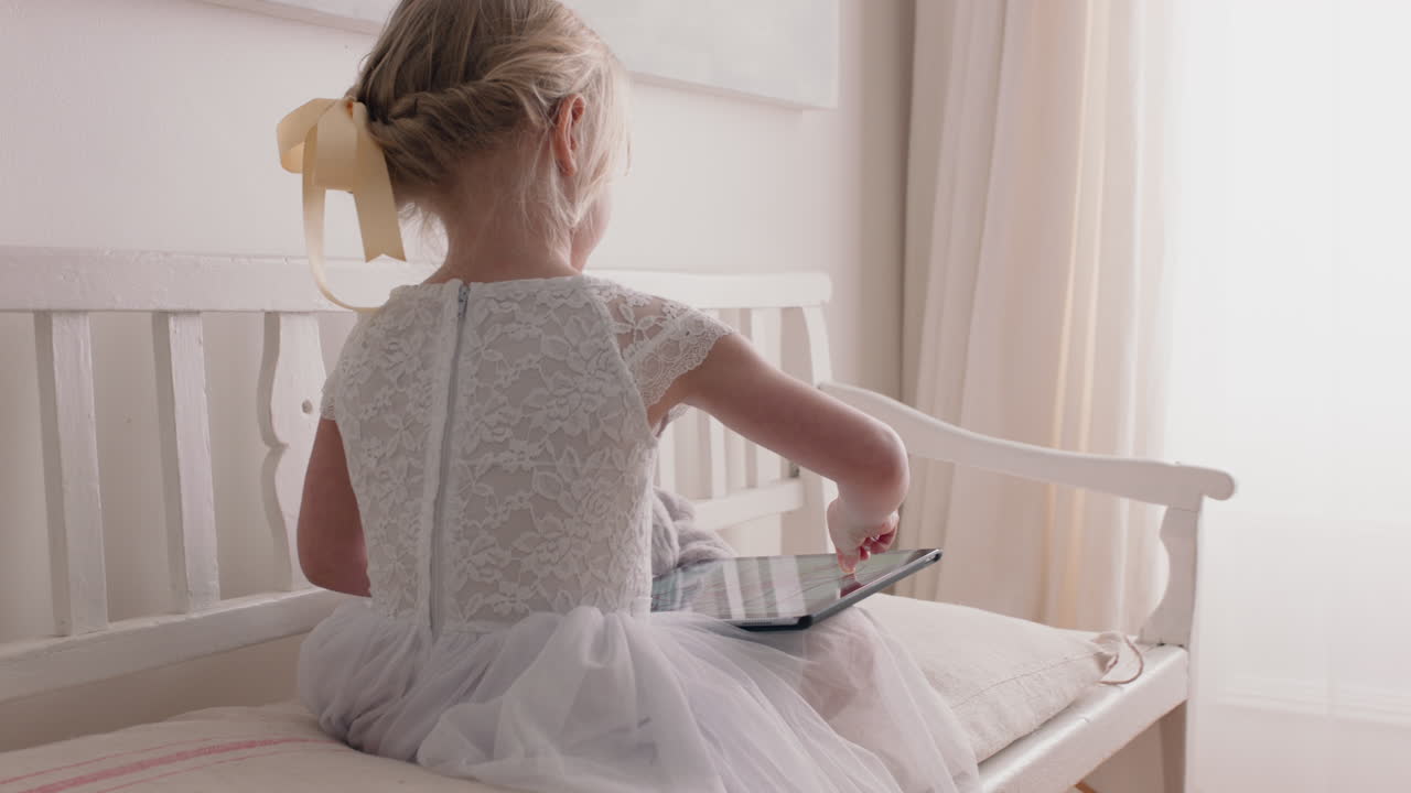 hermosa niña usando una tableta dibujando imágenes en la pantalla táctil disfrutando de la creatividad sentada en un banco con un oso de peluche comiendo piruleta en casa