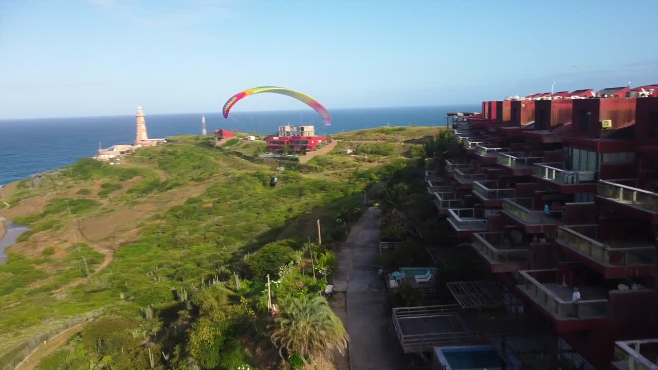 parapenteando sobre una ciudad costera con un faro y colinas verdes exuberantes