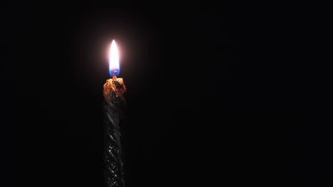 a single candle is lit on a black background. candle flame in the dark