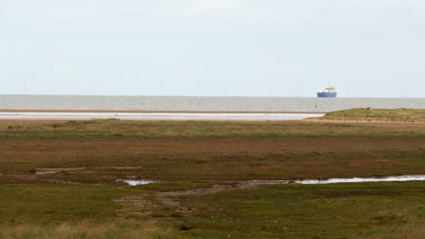 Wide-shot-of-tidal-mud-flats-with-Sea-and-cargo-ship-in-background-at-Saltfleet,-Louth,-Lincolnshire