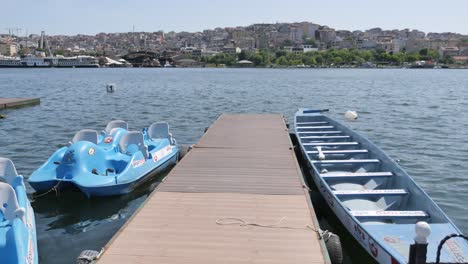 a wooden dock with a blue pedal boat and a dragon boat on a lake with a city in the background