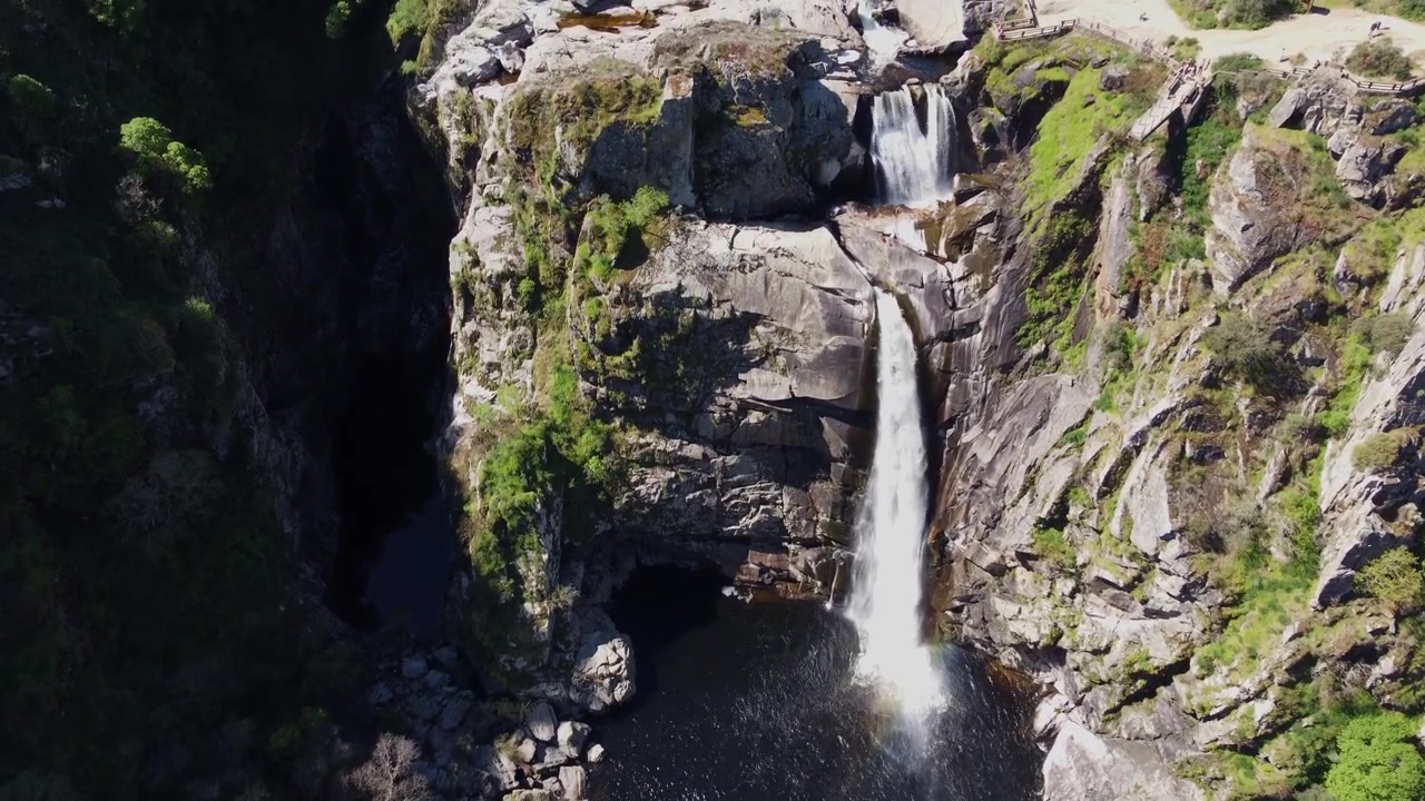 Spettacolare discesa di un drone 4K con inclinazione della telecamera verso l'alto, che rivela la magnifica cascata Pozo de los Humos che si getta in una scura pozza rocciosa a Salamanca, Spagna, in una luminosa giornata di sole.