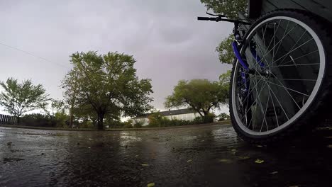 Bike-leaning-up-against-a-blue-wooden-fence-in-the-driveway-of-a-house-on-a-rainy-day