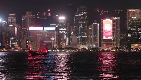 a boat sails past illuminated city skyline