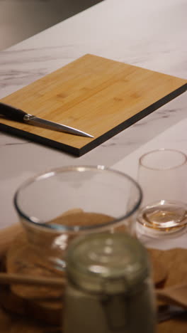 vertical video close up of wooden chopping board and knife on marble counter in kitchen ready to prepare ingredients for meal