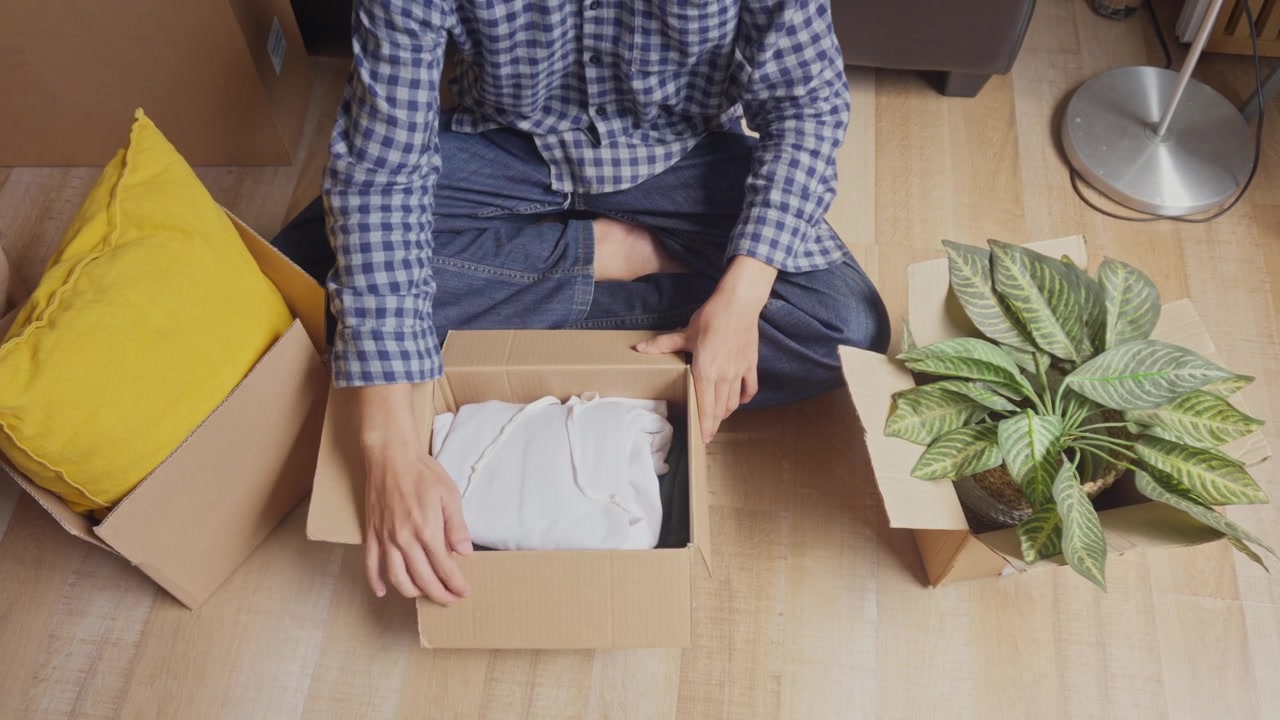 Close-up of person unboxing personal items and clothes from parcel on floor as part of moving