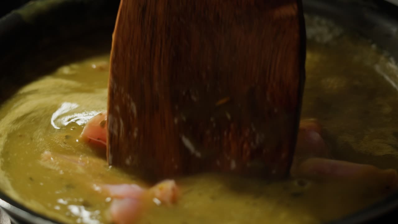Green boiling sauce with chicken texture close-up macro. Cooking green chicken curry with spices by wooden spoon at home.