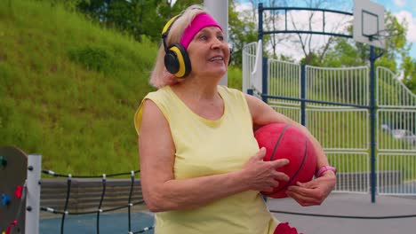 abuela mayor después del entrenamiento de baloncesto sentada escuchando música en la cancha del patio de recreo