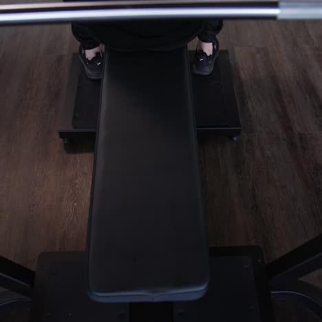 Handsome guy training on a modern sports equipment. Young athlete starts doing exercise on a simulator in gym. Muscular man exercising in fitness center. Top view